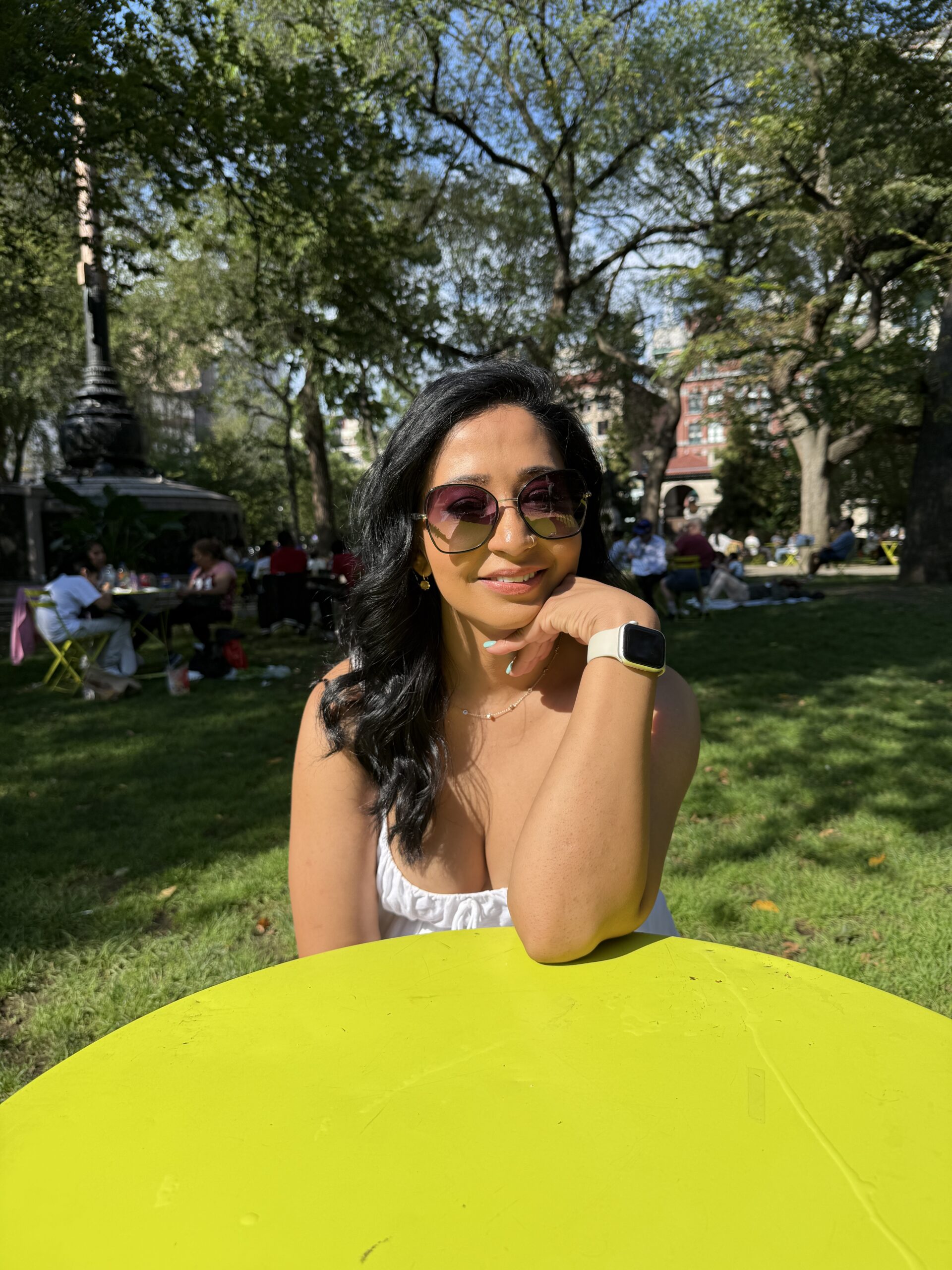 Career coach Rosey Singh sitting thoughtfully at yellow table in city park, representing strategic career planning and decision-making