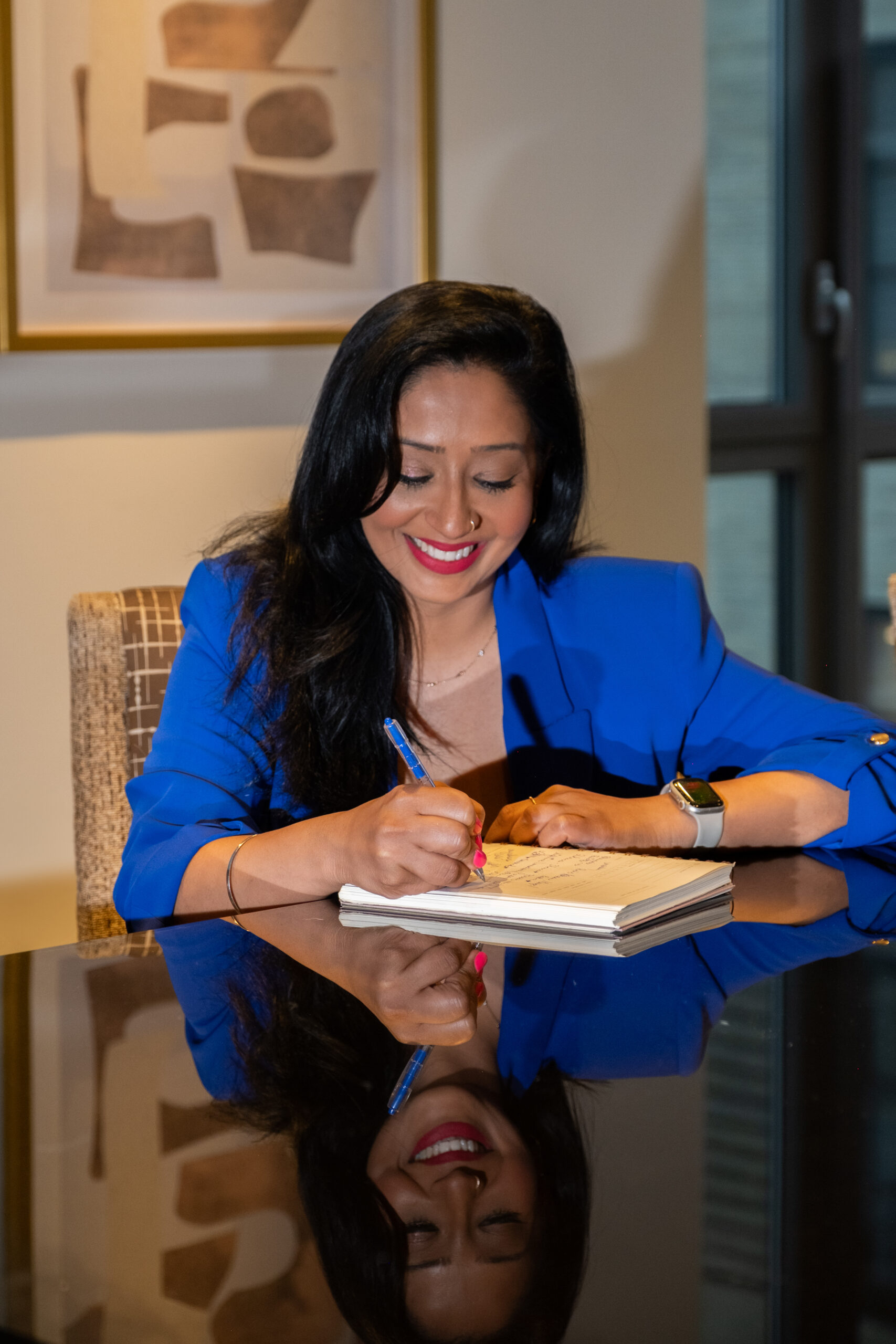 Rosey, founder of Eunioa and career consultant, smiling while writing in a notebook at a reflective desk, wearing a blue blazer