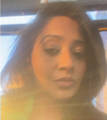 Woman with dark wavy hair in soft natural light with golden sun flare washing over the image, creating a dreamy, reflective mood